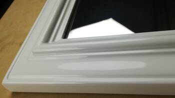 Detal narożnika białej ramy lustra w wysokim połysku — profilowana listwa odbijająca światło